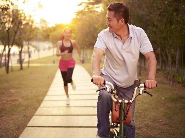 young asian couple running, riding bike outdoors in park at sunset, fitness, sport and exercise, healthy life and lifestyle concept.